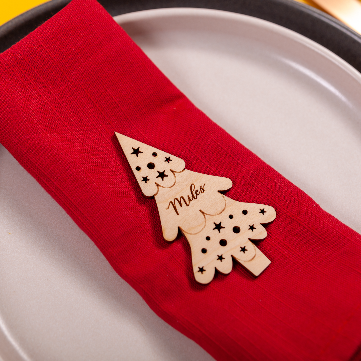 Wooden Christmas tree-shaped napkin holder on a red napkin over a white plate.
