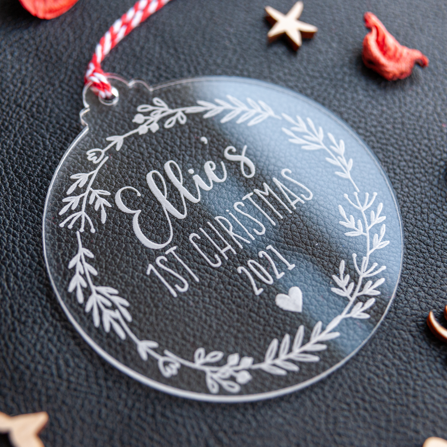 Close-up of laser-etched “Baby’s First Christmas” acrylic ornament showing frosted engraving and satin red ribbon.