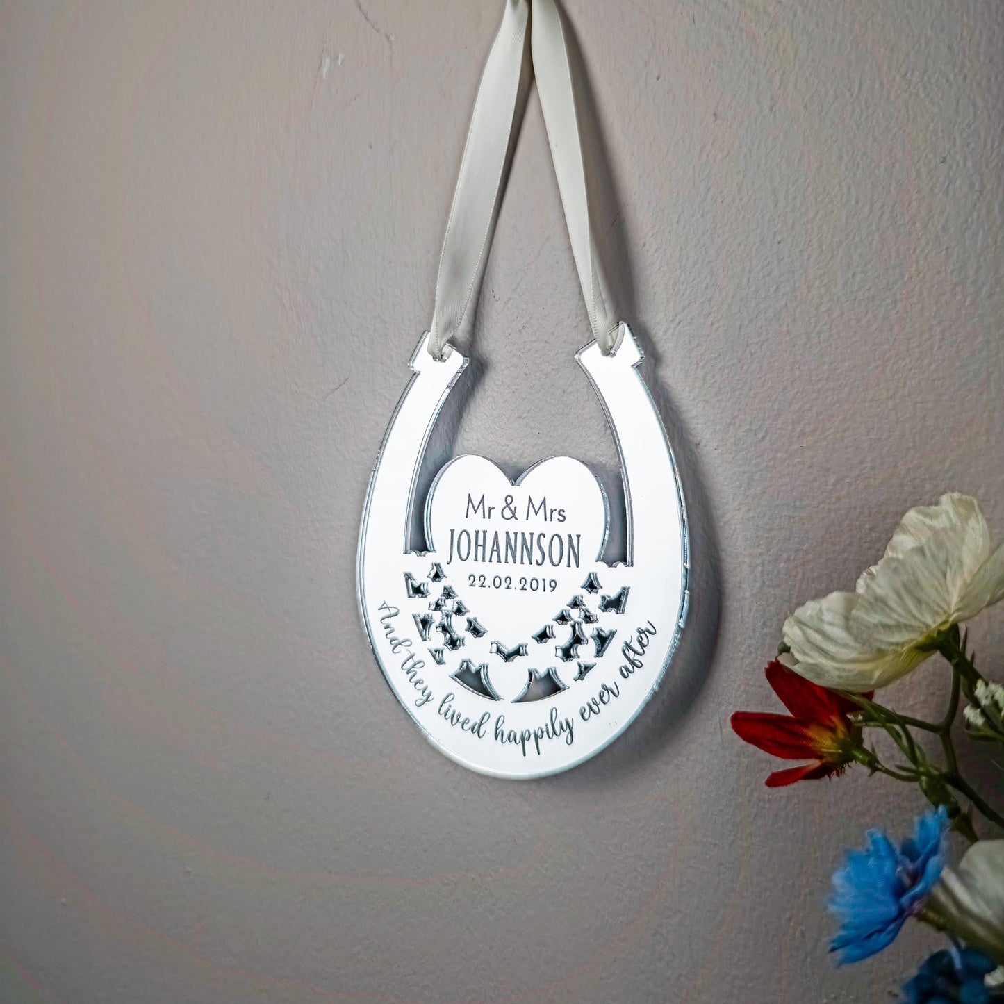 Decorative horseshoe with engraved text on a gray wall with flowers.