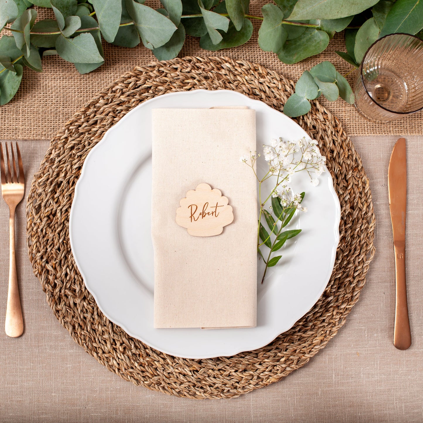 Table setting with white plates, gold cutlery, and a woven placemat.