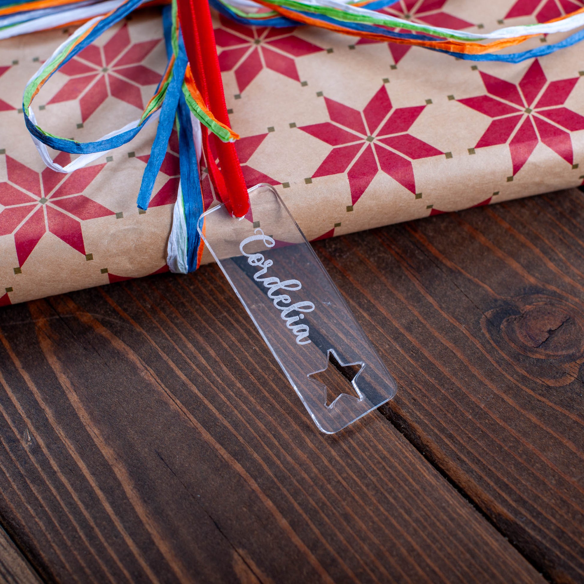 Gift wrapped in star-patterned paper with colorful ribbons on a wooden surface, featuring a 'Cordelia' tag.