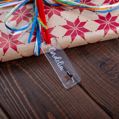 Gift wrapped in star-patterned paper with colorful ribbons on a wooden surface, featuring a 'Cordelia' tag.