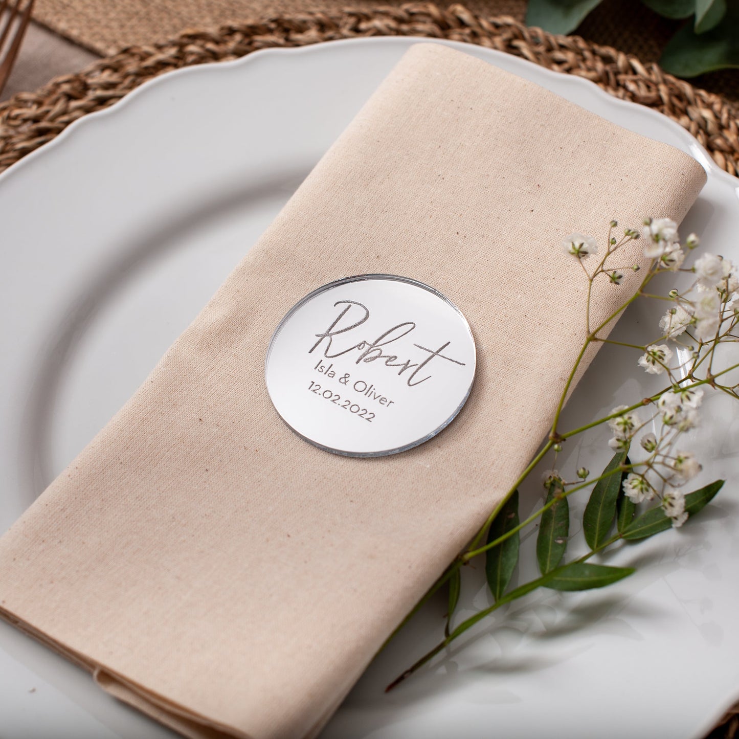 Napkin with a name tag on a white plate with flowers, on a woven placemat.