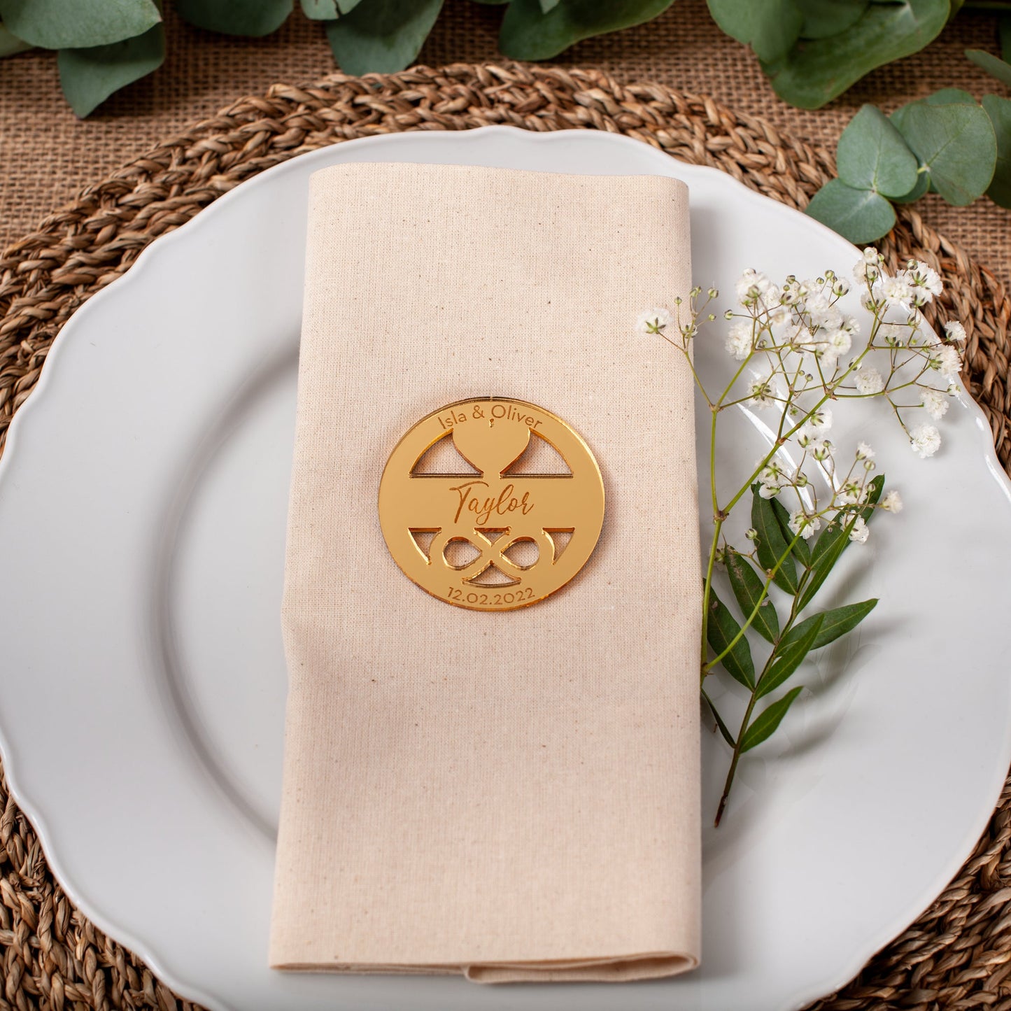 Table setting with a gold place card, beige napkin, and white plate on a woven placemat.