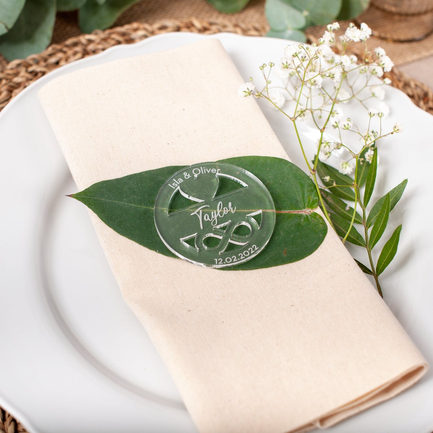 Napkin with a decorative leaf and floral arrangement on a white plate, set on a woven placemat.