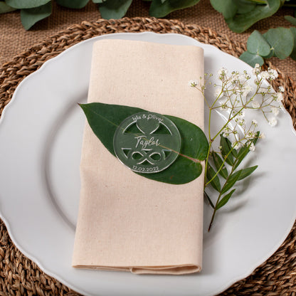 Table setting with a white plate, beige napkin, green leaf, and small white flowers on a woven placemat.