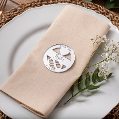 Folded beige napkin with a decorative metal clip on a white plate, placed on a woven placemat.