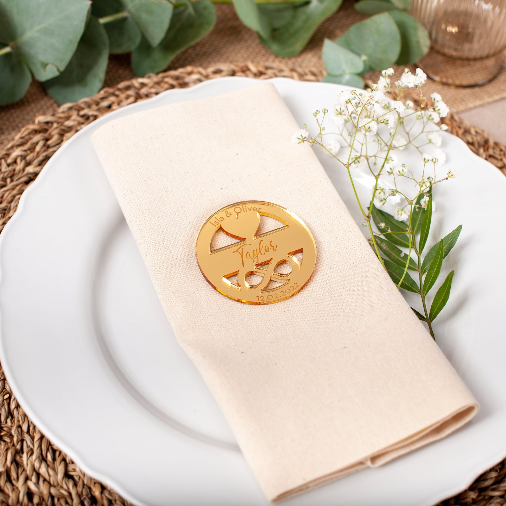 Napkin with a decorative emblem on a white plate with greenery, placed on a woven placemat.