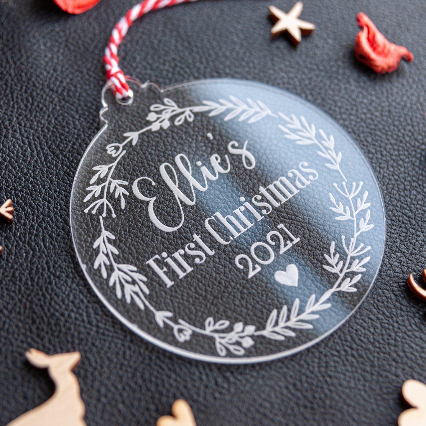 Clear acrylic first Christmas bauble with floral wreath and red and white twine