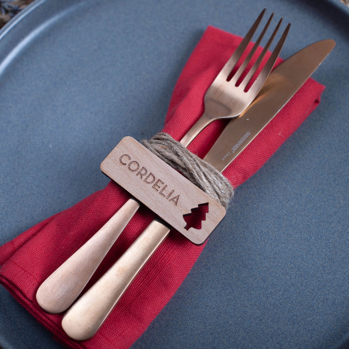 Flat-lay of personalised wooden Christmas place settings arranged on festive table linen