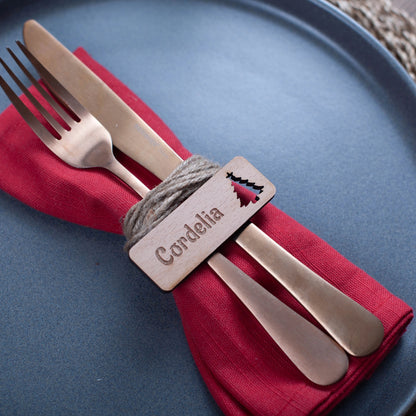 Flat-lay of wooden Christmas name tags placed beside pine sprigs and baubles