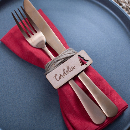 Flat-lay of engraved wooden Christmas labels styled with silver cutlery and greenery