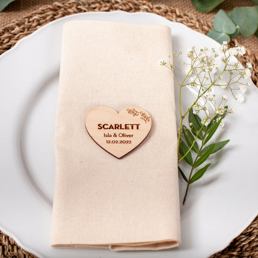Napkin with a heart-shaped wooden name tag on a white plate with a woven placemat.