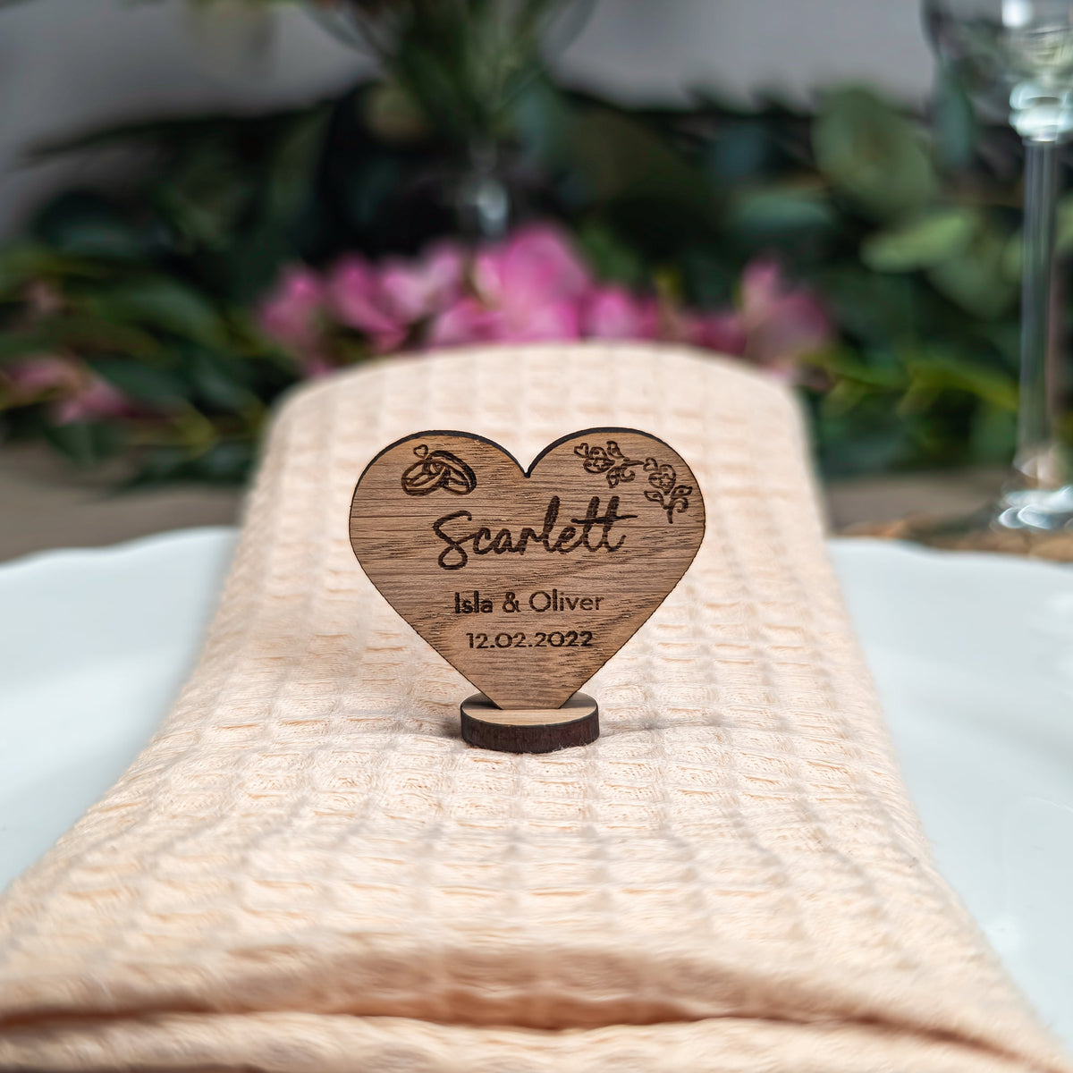 Wooden heart-shaped place card with engraved text on a white plate with a beige napkin.