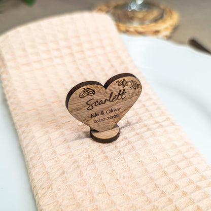 Wooden heart-shaped place card holder on a white plate with a beige napkin