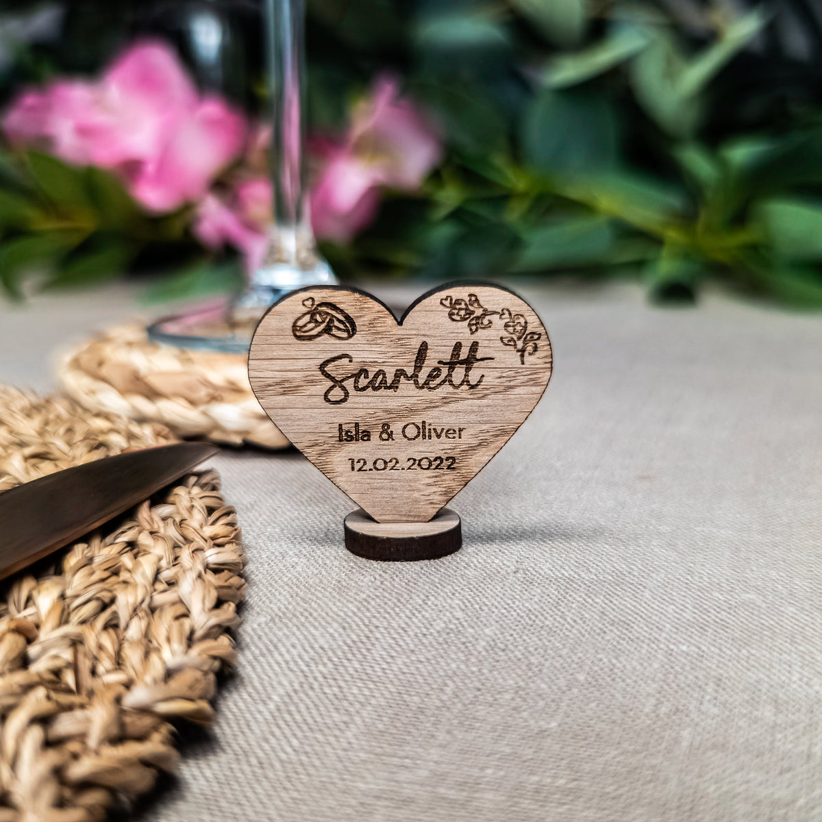 Wooden heart-shaped decoration with engraved names and date on a table setting.