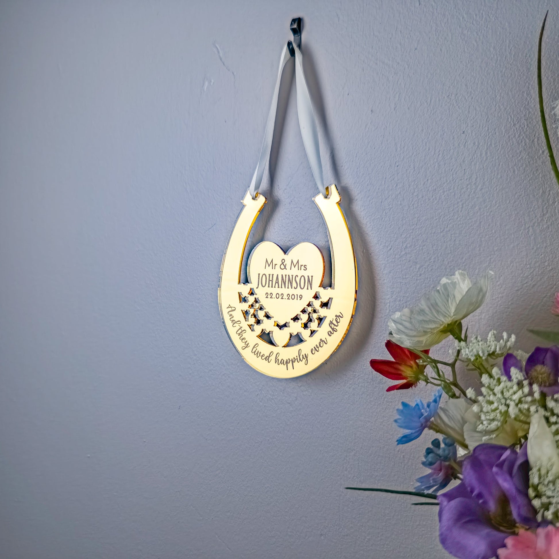 Decorative gold horseshoe with engraved text on a gray wall with flowers.