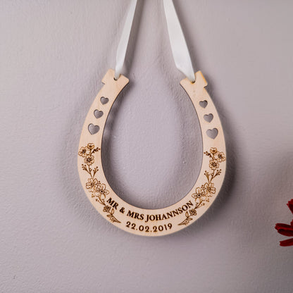 Wooden horseshoe with engraved text and floral designs on a gray background