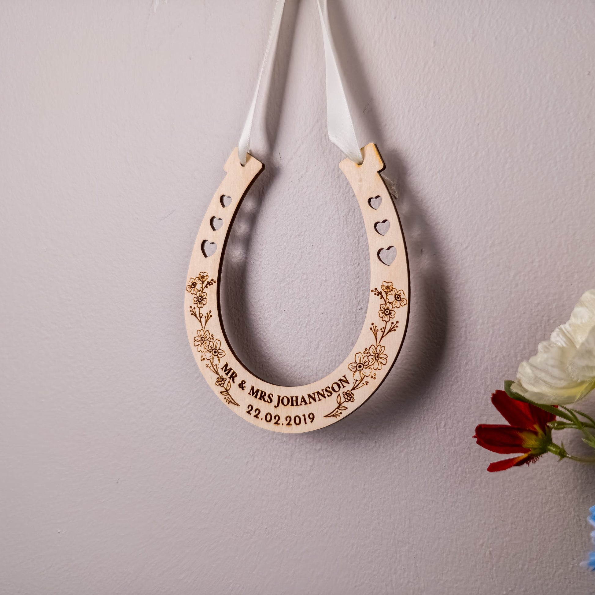 Decorative wooden horseshoe with engraved text on a plain wall with flowers.