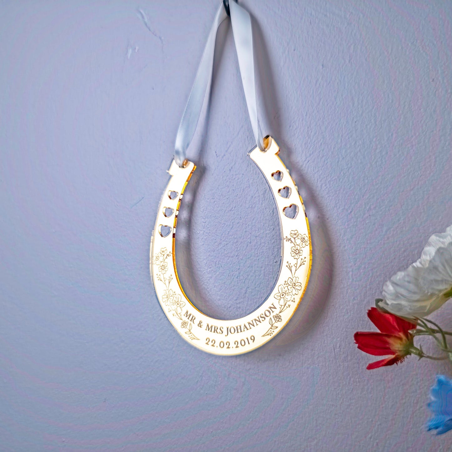 Decorative gold horseshoe with engraved text on a light purple wall with flowers.