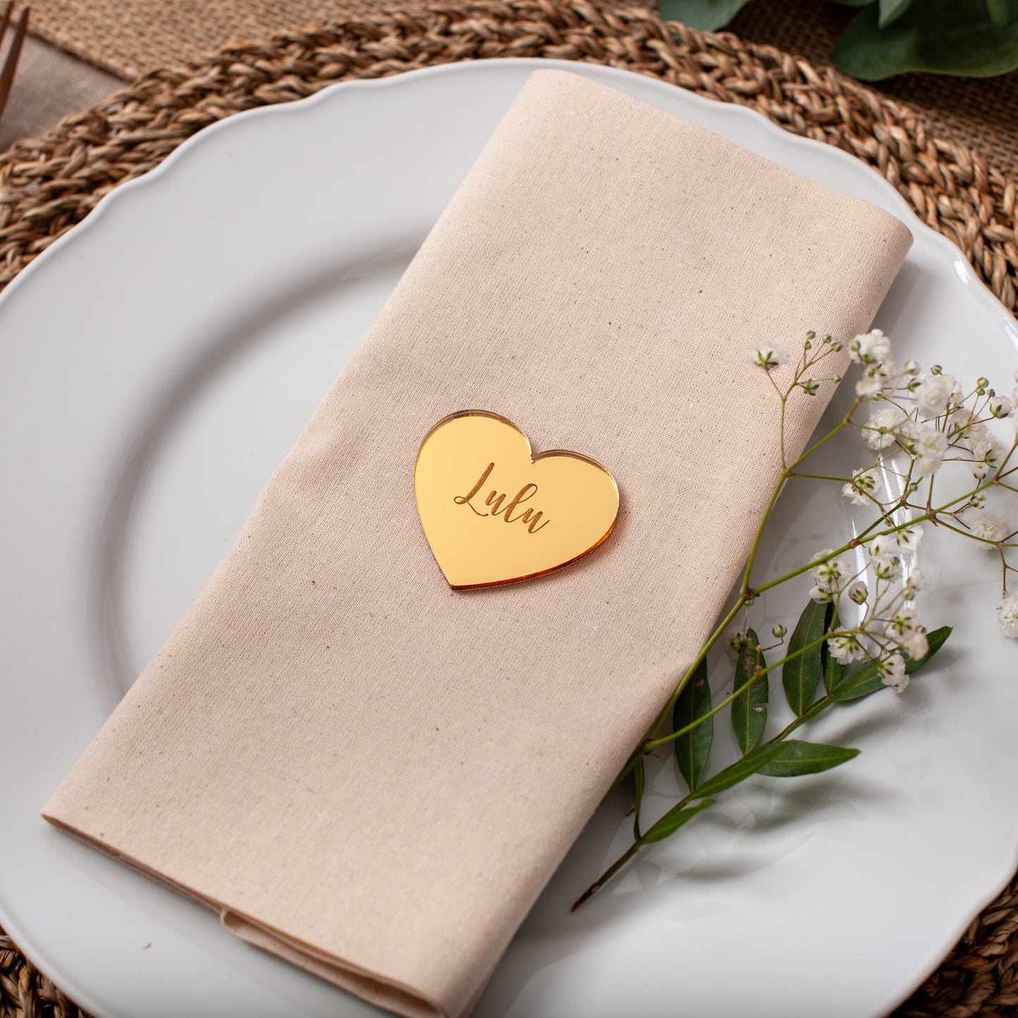 Napkin with a heart-shaped name tag on a white plate with a woven placemat.