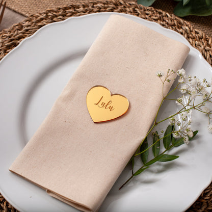 Napkin with a heart-shaped name tag on a white plate with a woven placemat.