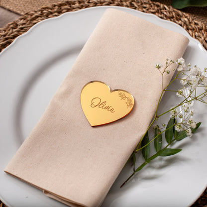Napkin with a heart-shaped name tag on a plate with a decorative leaf and flowers.