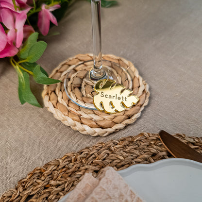 Wine glass with a decorative coaster and name tag on a table setting with flowers.