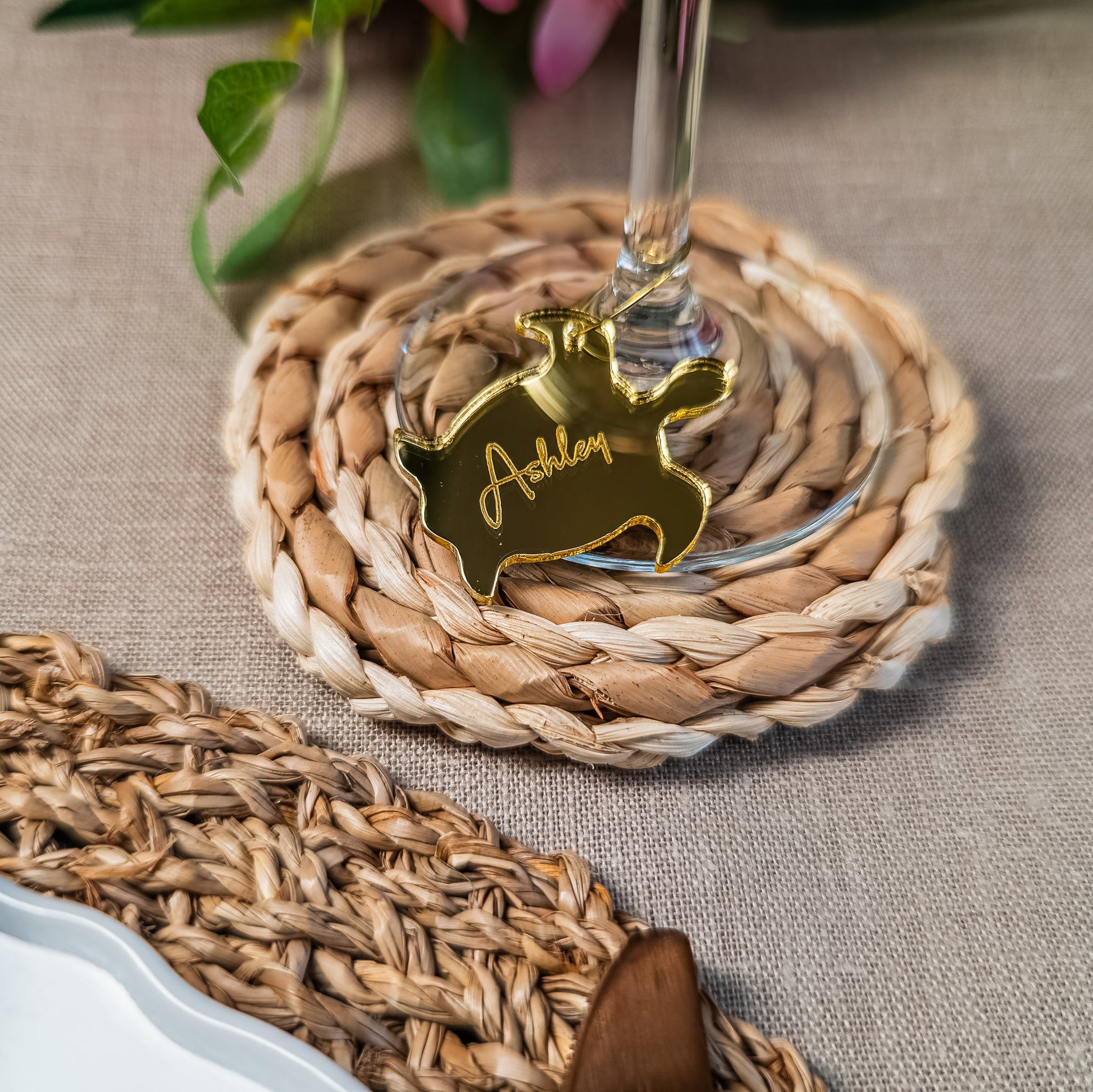 Gold sea turtle coaster with engraved name, placed on a woven coaster with a glass of wine.