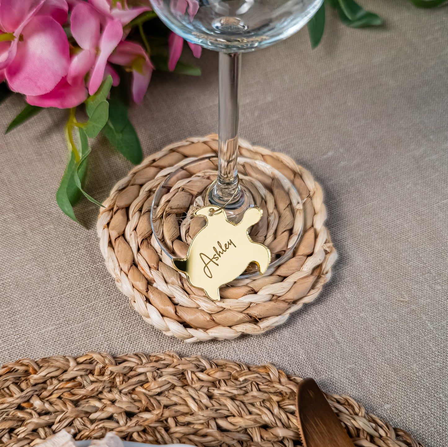 Wine glass with a decorative coaster on a textured surface with pink flowers in the background