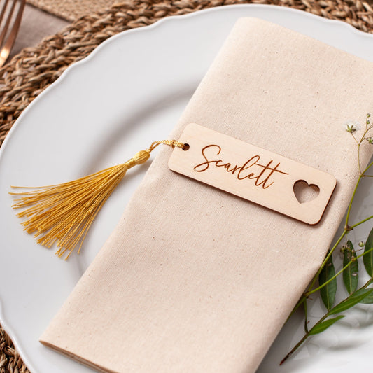 Napkin with a name tag on a white plate with greenery, placed on a woven mat.