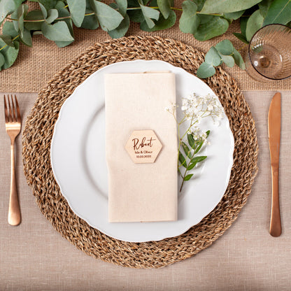Elegant table setting with a woven placemat, white plate, gold cutlery, and greenery.