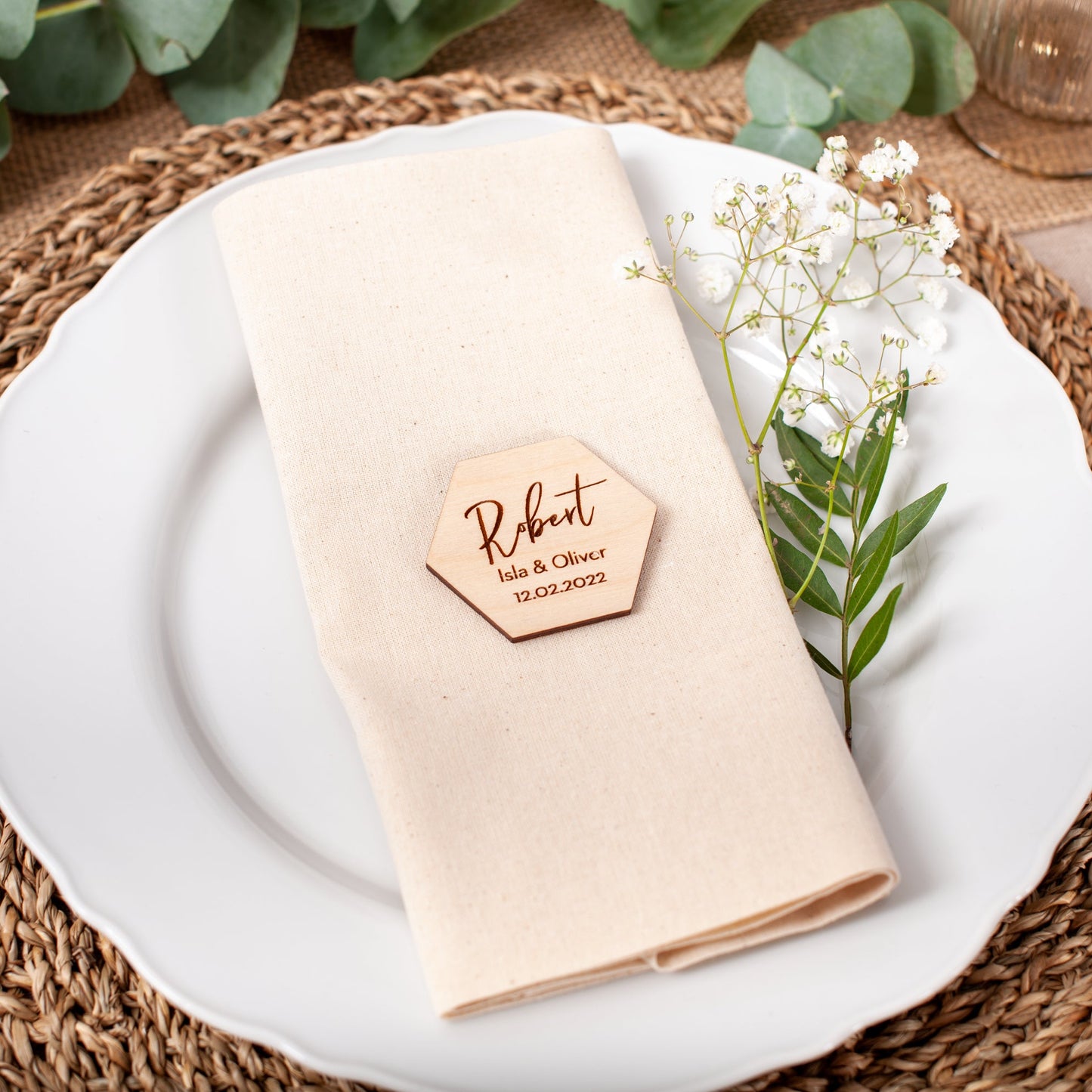 Place setting with a folded beige napkin, wooden name card, and white plate on a woven placemat.