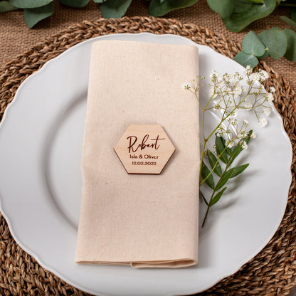 Place setting with a folded beige napkin, wooden name card, and white flowers on a woven placemat.