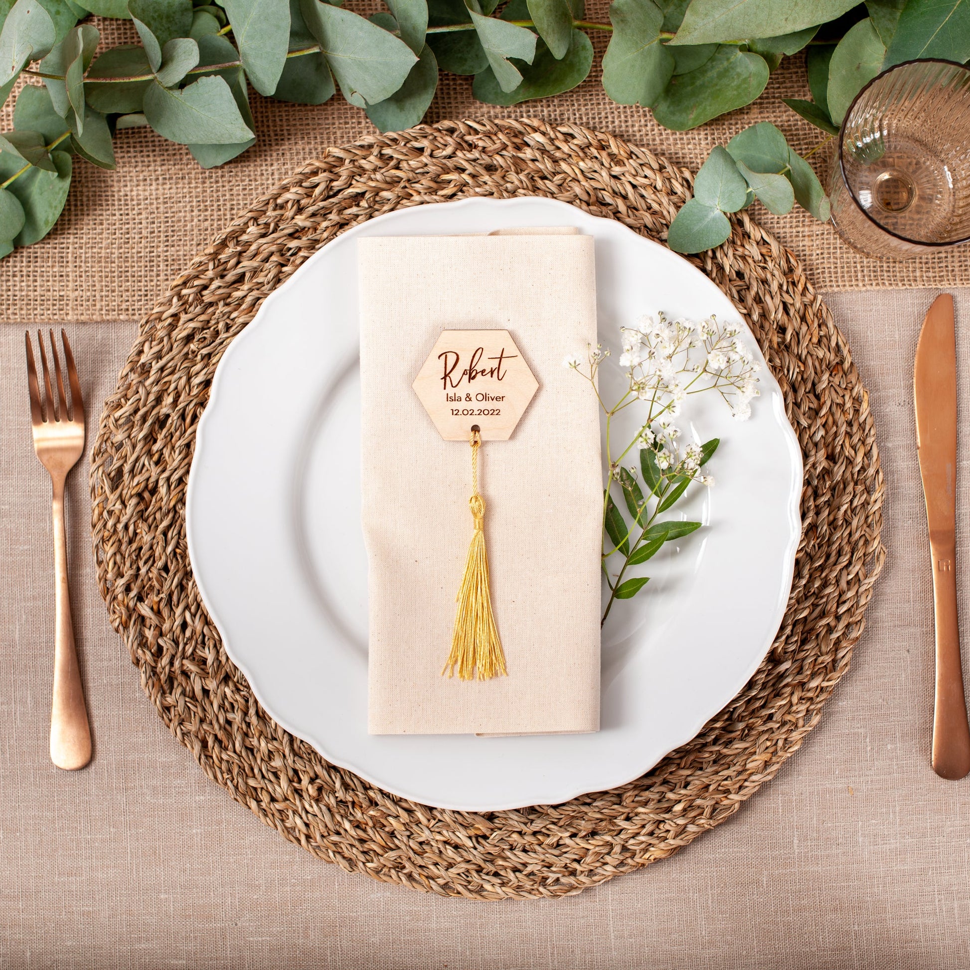 Dining table setting with woven placemat, white plate, gold cutlery, and decorative napkin.