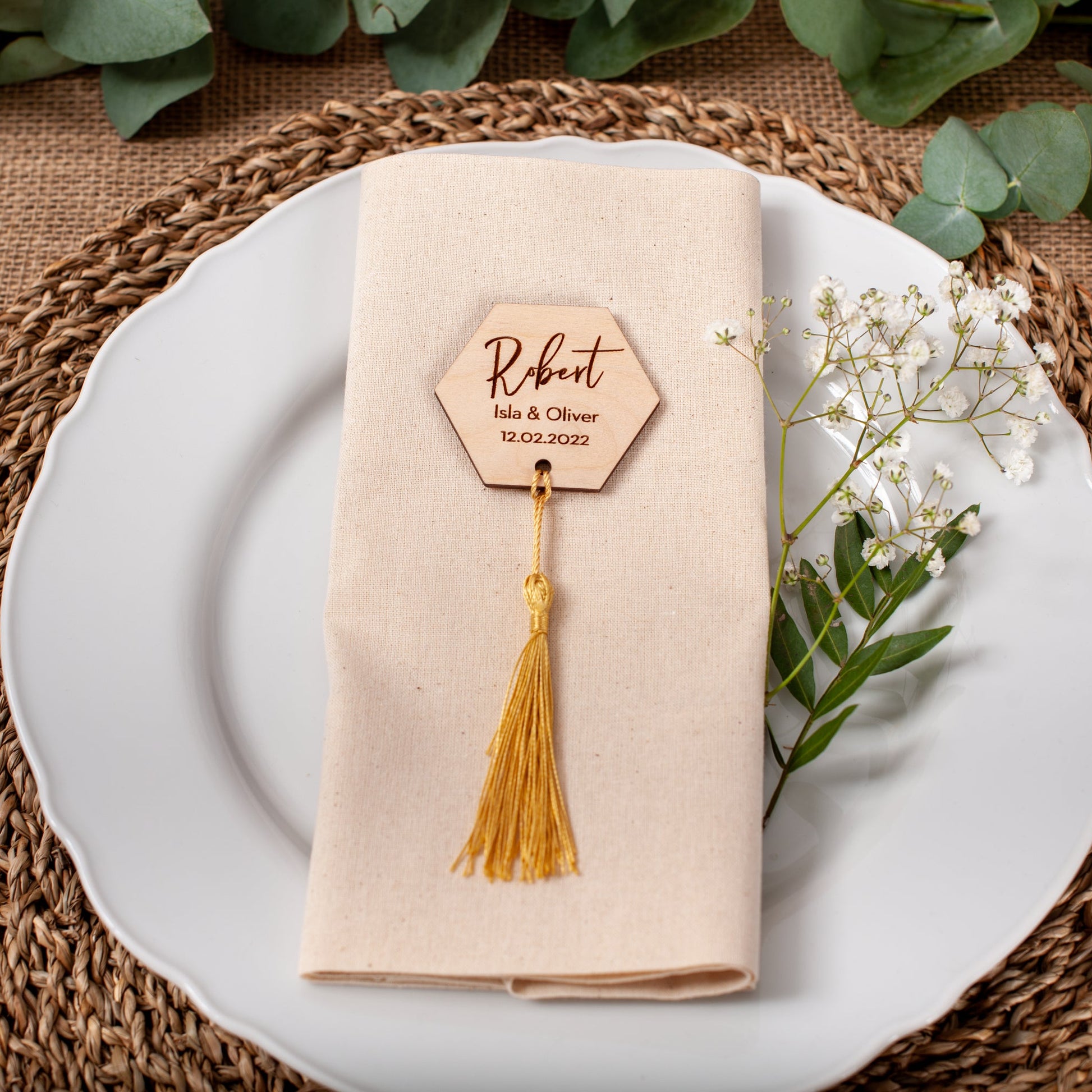 Place setting with a beige napkin, name tag, and white flowers on a woven placemat.