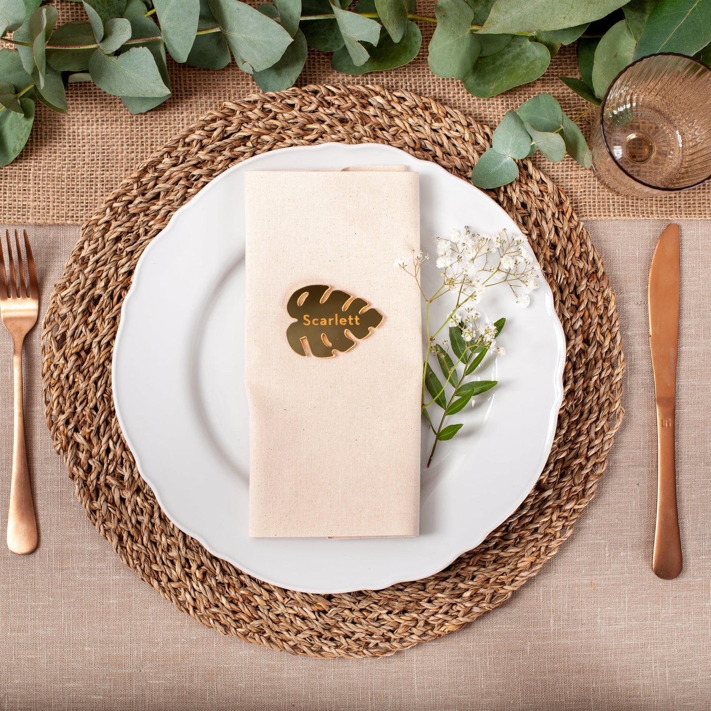 Table setting with white plates, gold cutlery, and a woven placemat on a brown tablecloth.